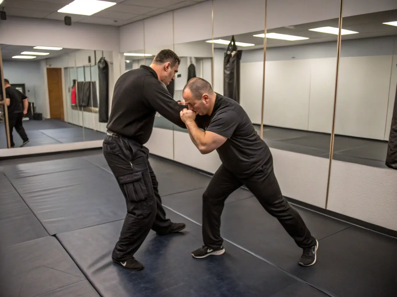 A photograph of a Krav Maga instructor demonstrating a technique to a student, highlighting the personalized attention and expert guidance provided at ACADEMIE DUBOC KRAV MAGA 27. The focus is on precision, control, and effective application of self-defense skills.